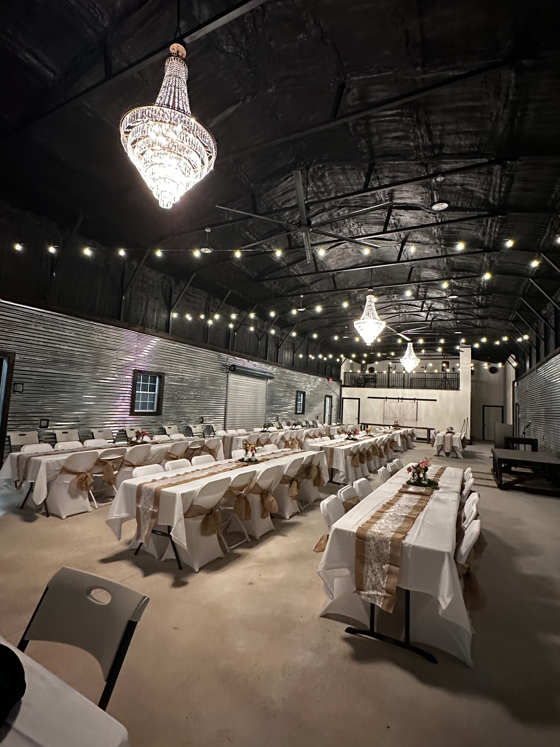 Elegant event hall with long banquet tables, white chair covers, string lights, and chandeliers