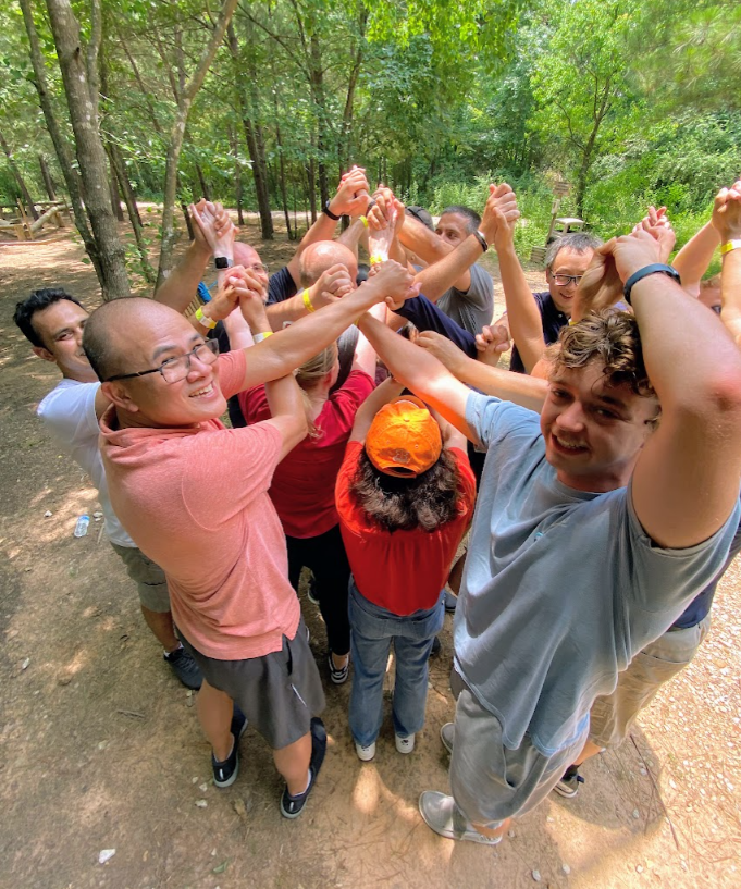 Group of people standing in a forest trail, raising arms together in a playful circle.