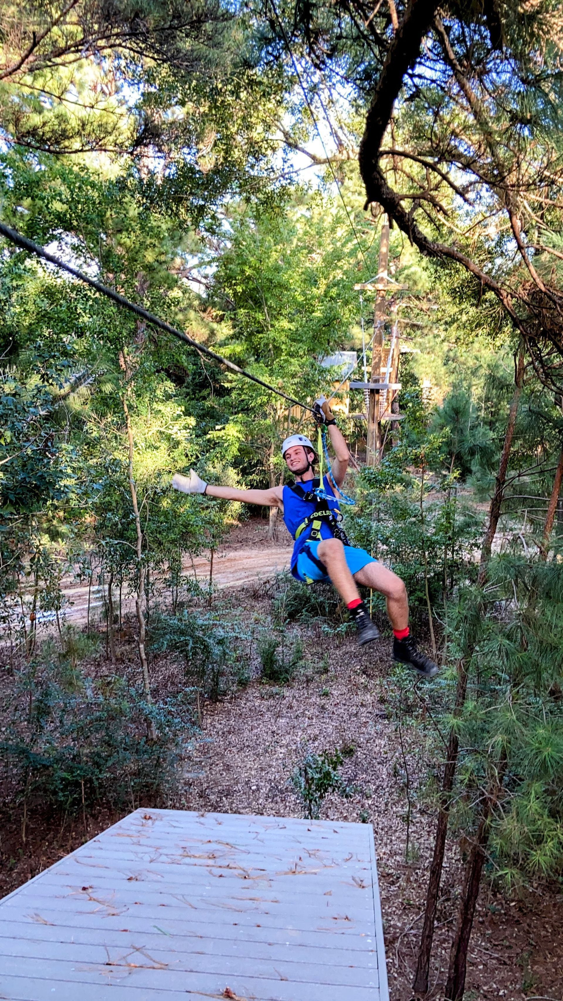 Person ziplining through a wooded outdoor course, wearing a blue harness and helmet