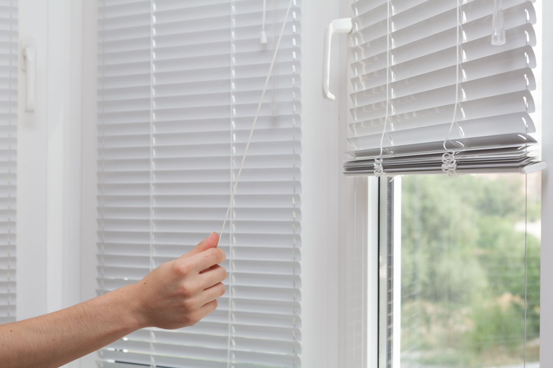 Girls raise the white blinds with a cord.
