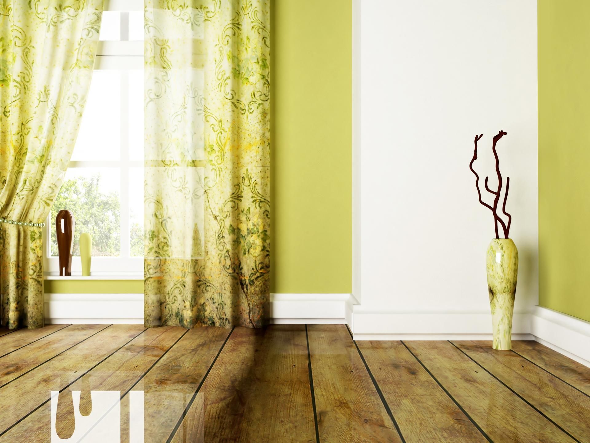 Empty room with hardwood floor, green walls, white trim, window with yellow curtains, vase with branches.