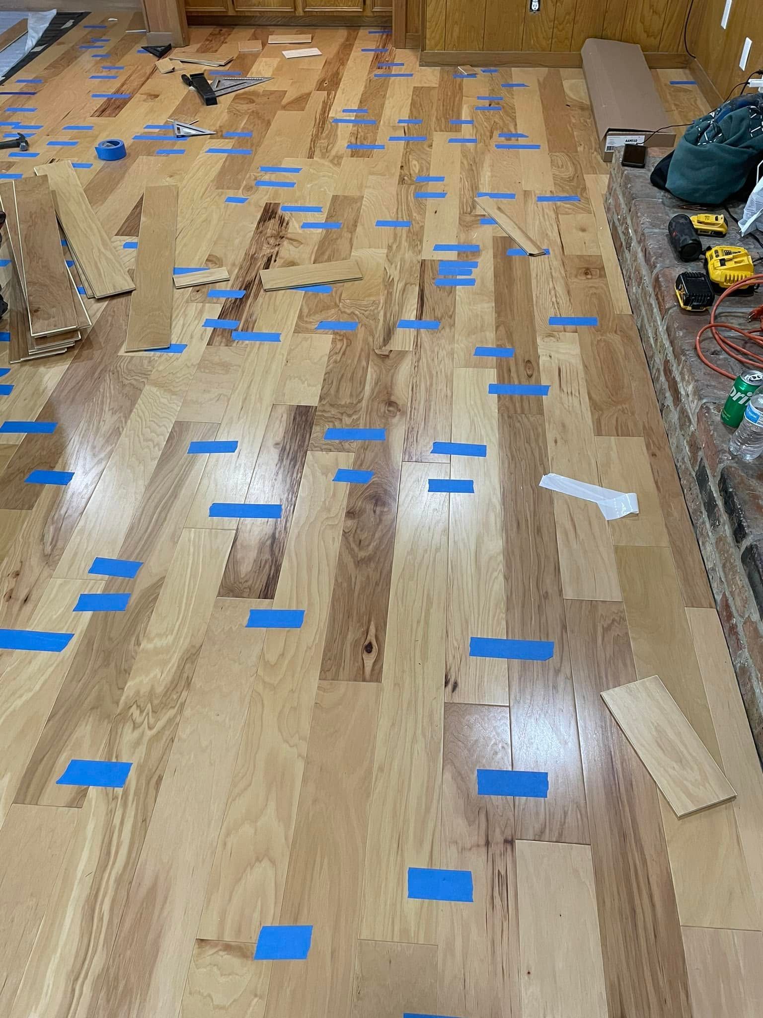 Wooden floor under construction with blue tape markers, scattered boards, and tools along the edges