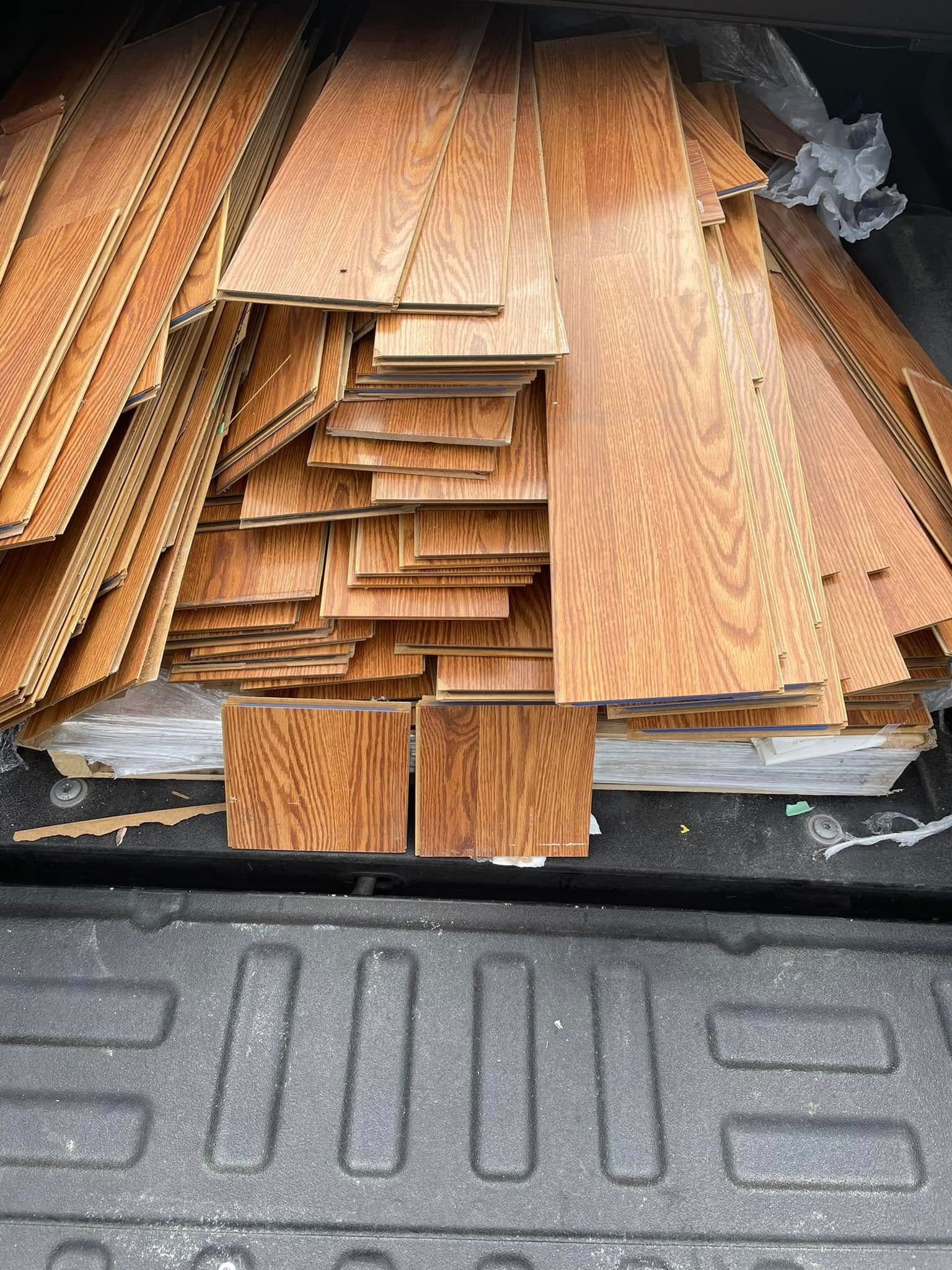 Stack of wooden planks and flooring boards in a truck bed, with black ribbed liner visible.