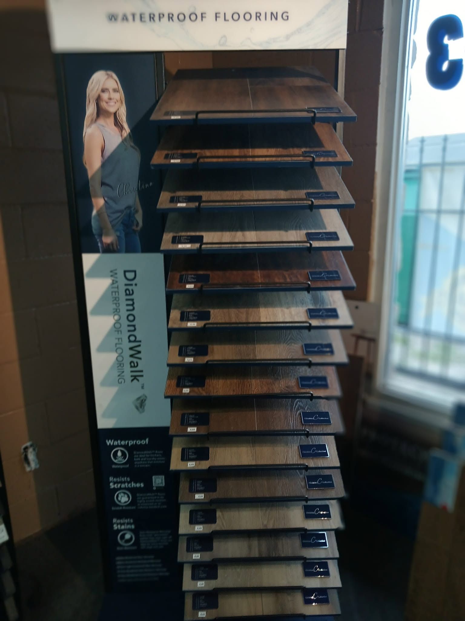 Display rack of waterproof flooring samples in a store, with a woman poster on the side.