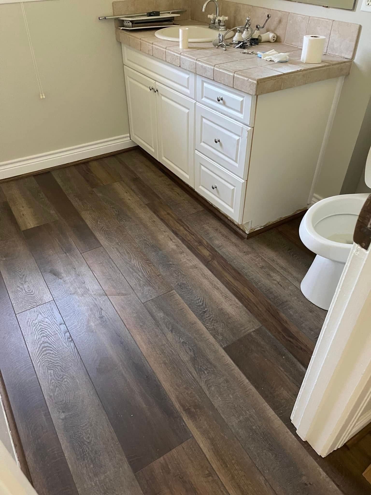 Bathroom with dark wood-look flooring, white vanity, and toilet near a doorway.