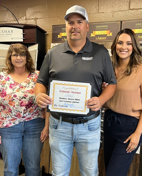 Three people indoors, with a man holding a certificate and two women standing beside him, smiling.