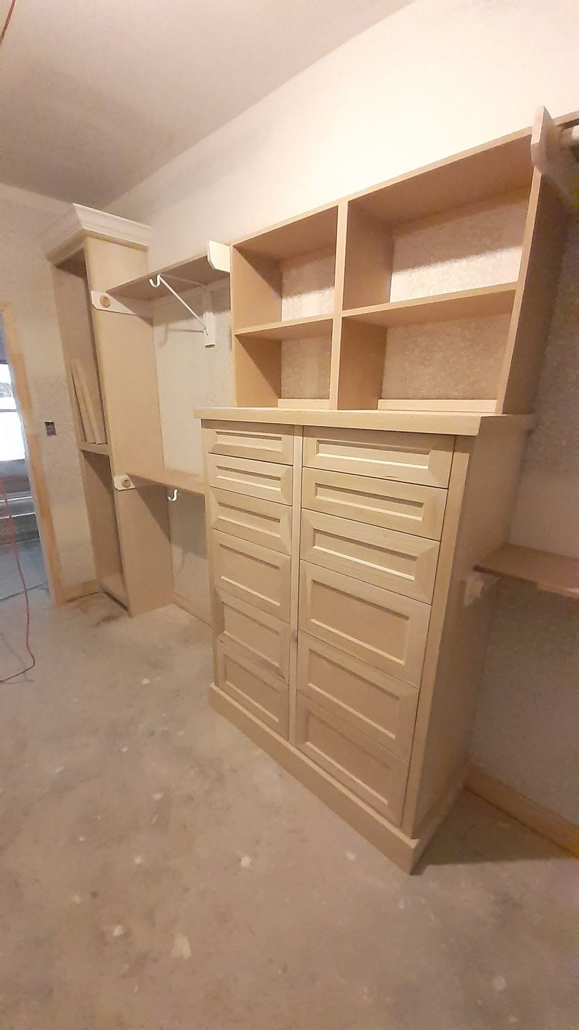 Built-in wooden shelving and cabinets in a closet under construction, unfinished room with drywall and dust.