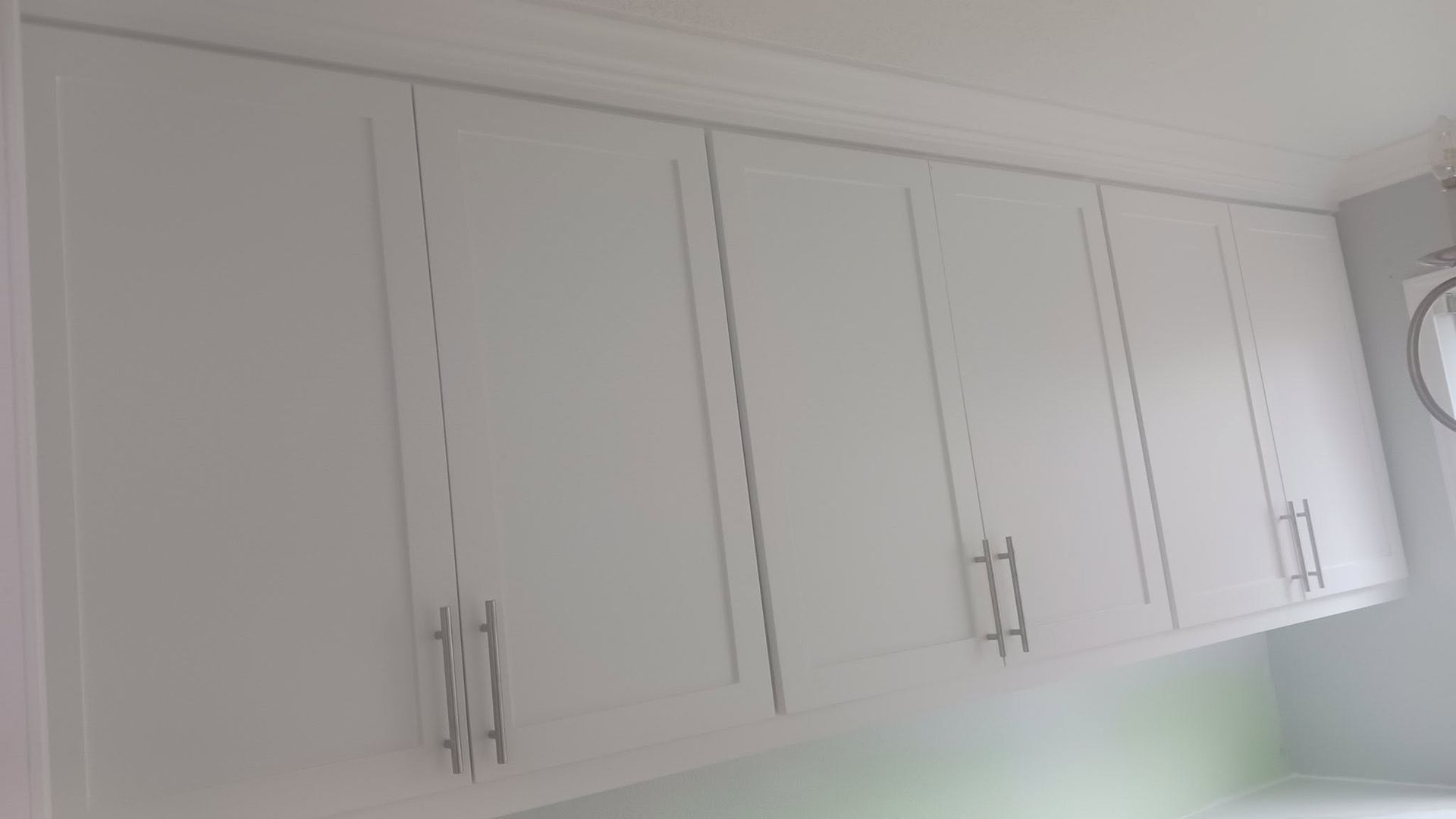 White kitchen cabinets with silver handles mounted on a wall above a countertop.