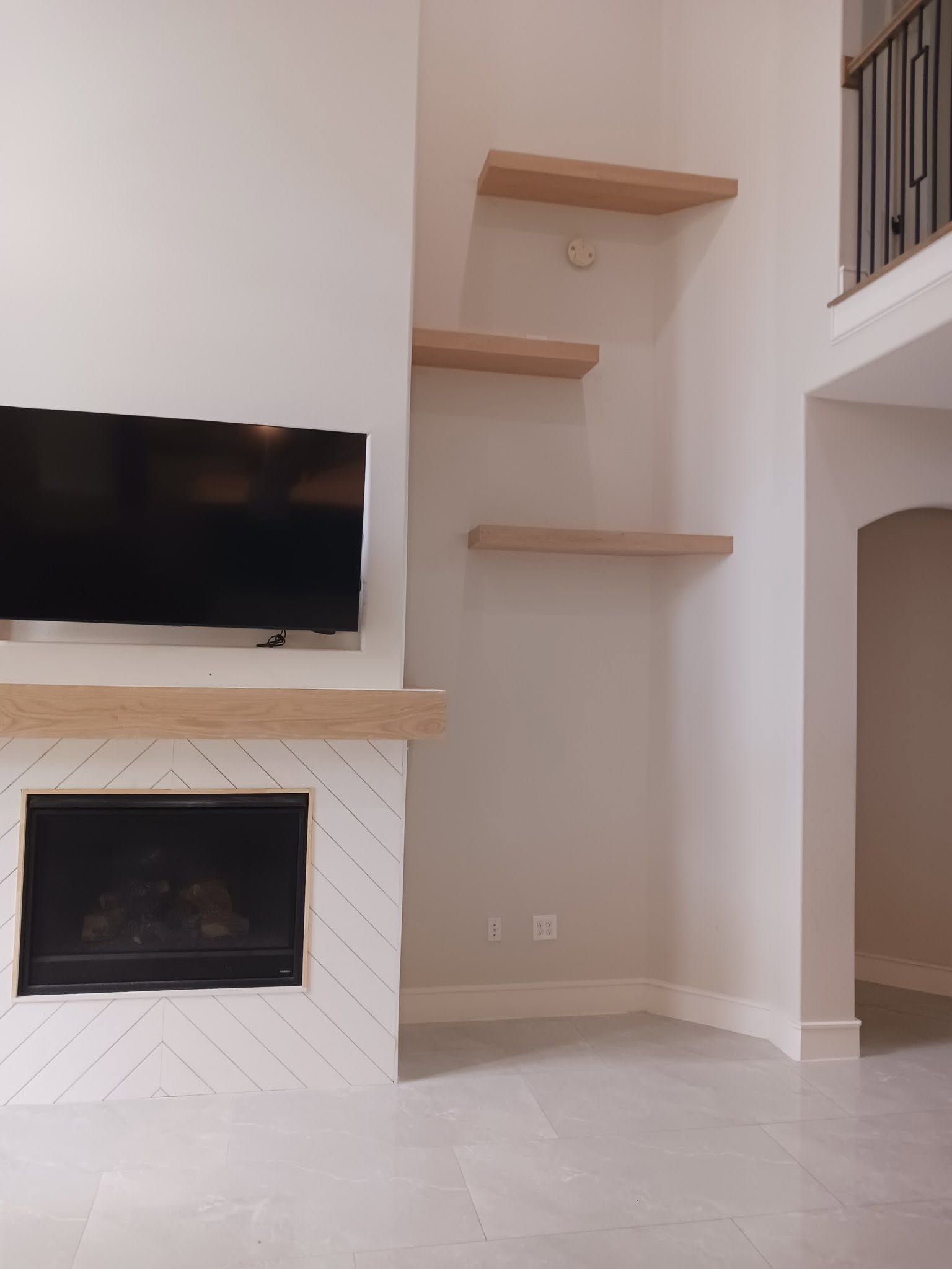 Modern living room corner with wall-mounted TV, fireplace, and floating shelves on a light tiled floor