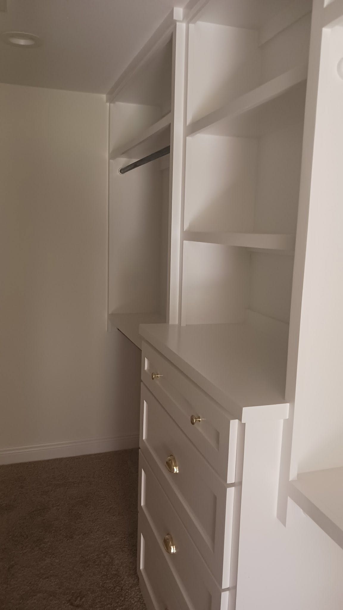 Empty walk-in closet with white shelves, drawers, and a hanging rod.