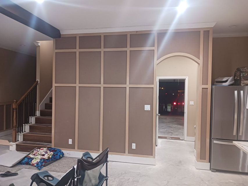 Unfinished room with wall framing, staircase, stainless fridge, and arched doorway to a dark outside view.