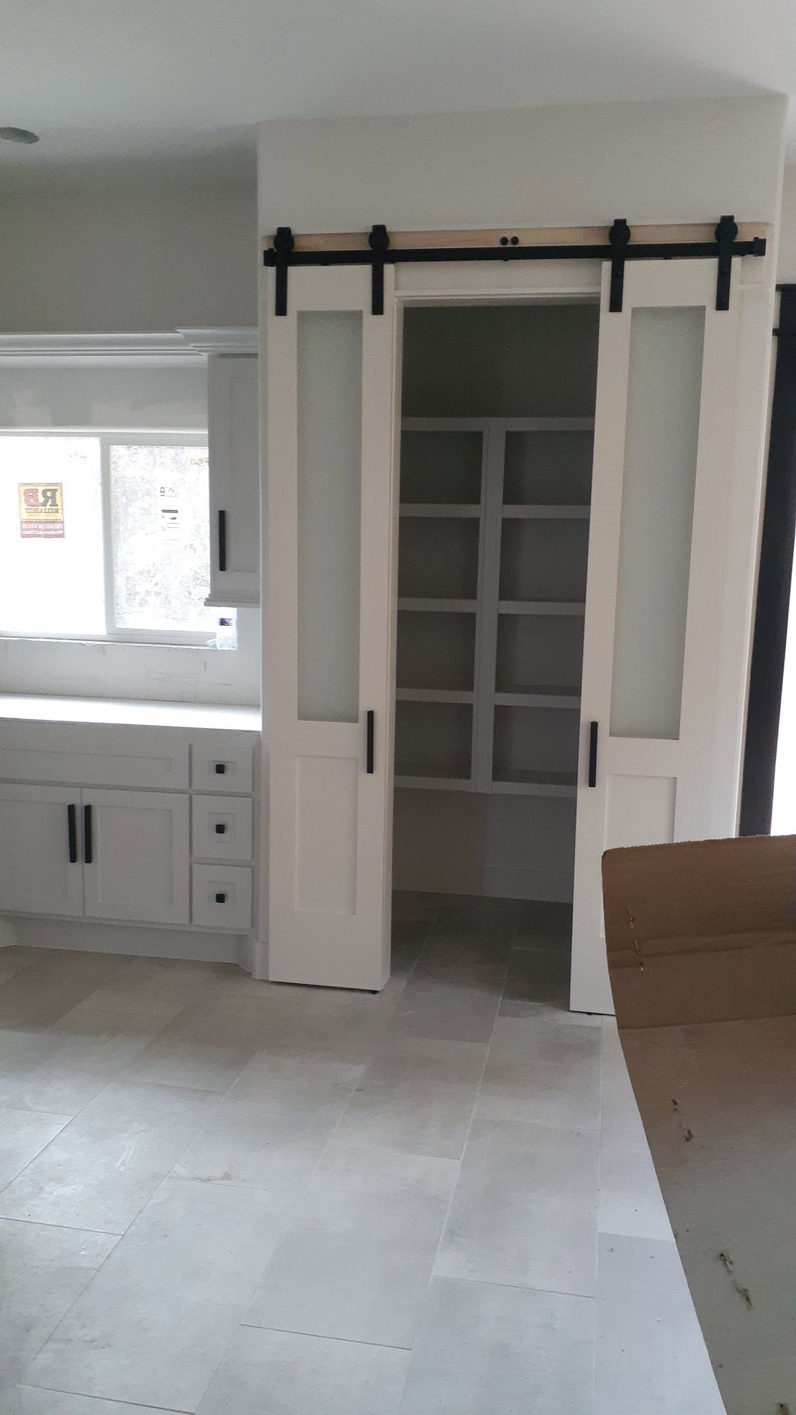 Sliding barn doors open to a pantry in a bright, modern kitchen