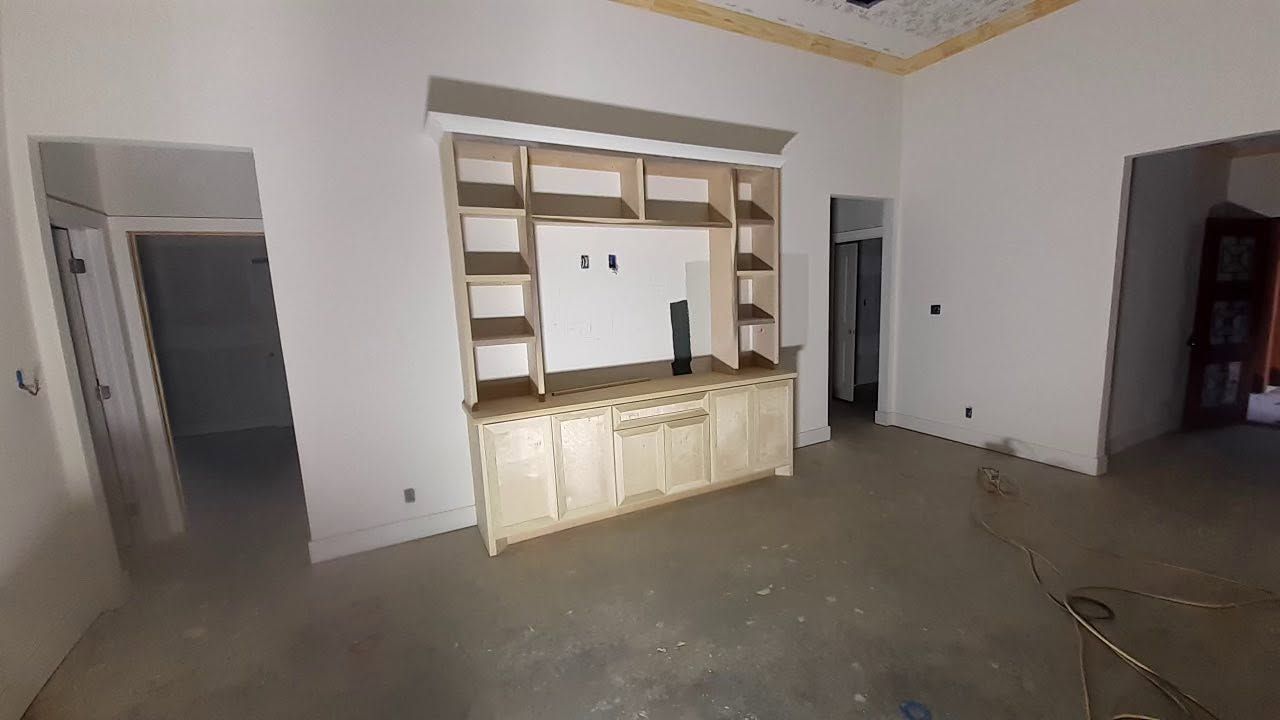 Empty room with white walls, built-in shelves, and a beige cabinet against the back wall.