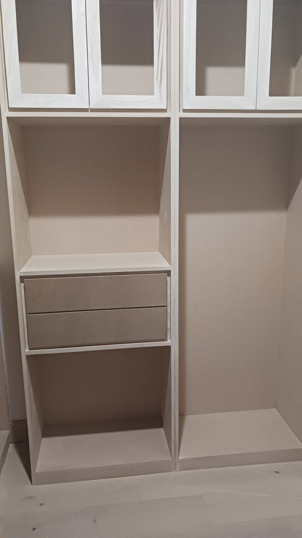 Built-in closet with white cabinets, shelves, and three drawers above an open lower section.