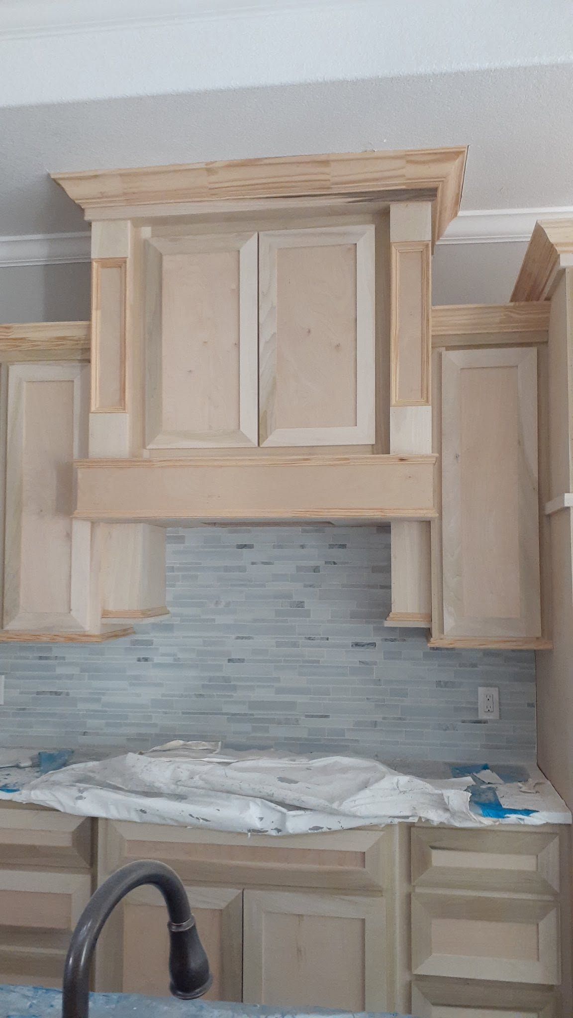 Unfinished kitchen cabinets above sink with white backsplash and countertop under construction