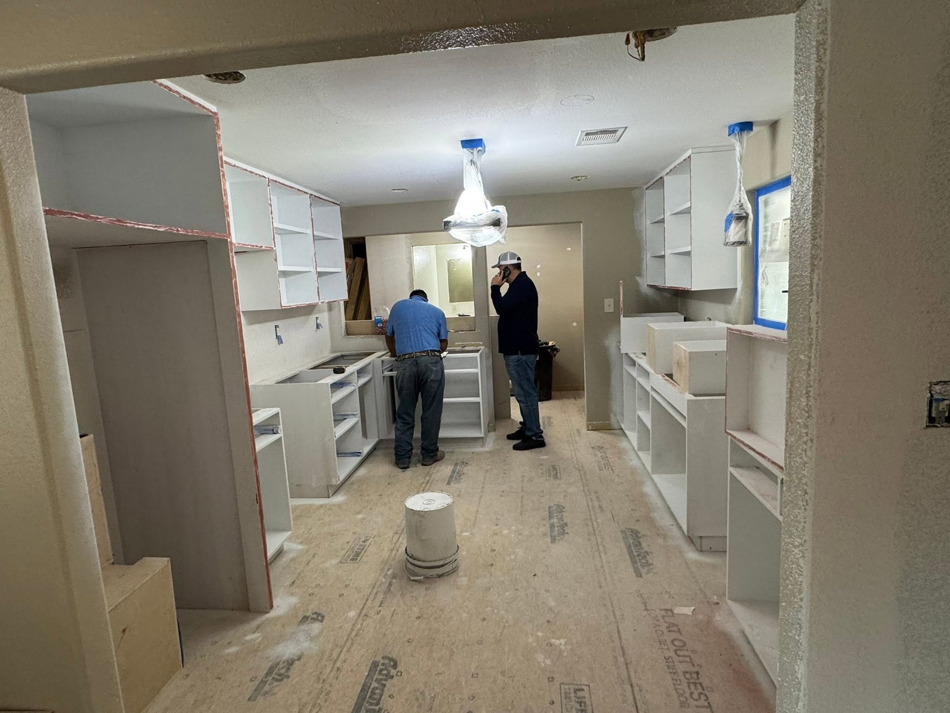 Kitchen under renovation with cabinets installed and two workers measuring the floor