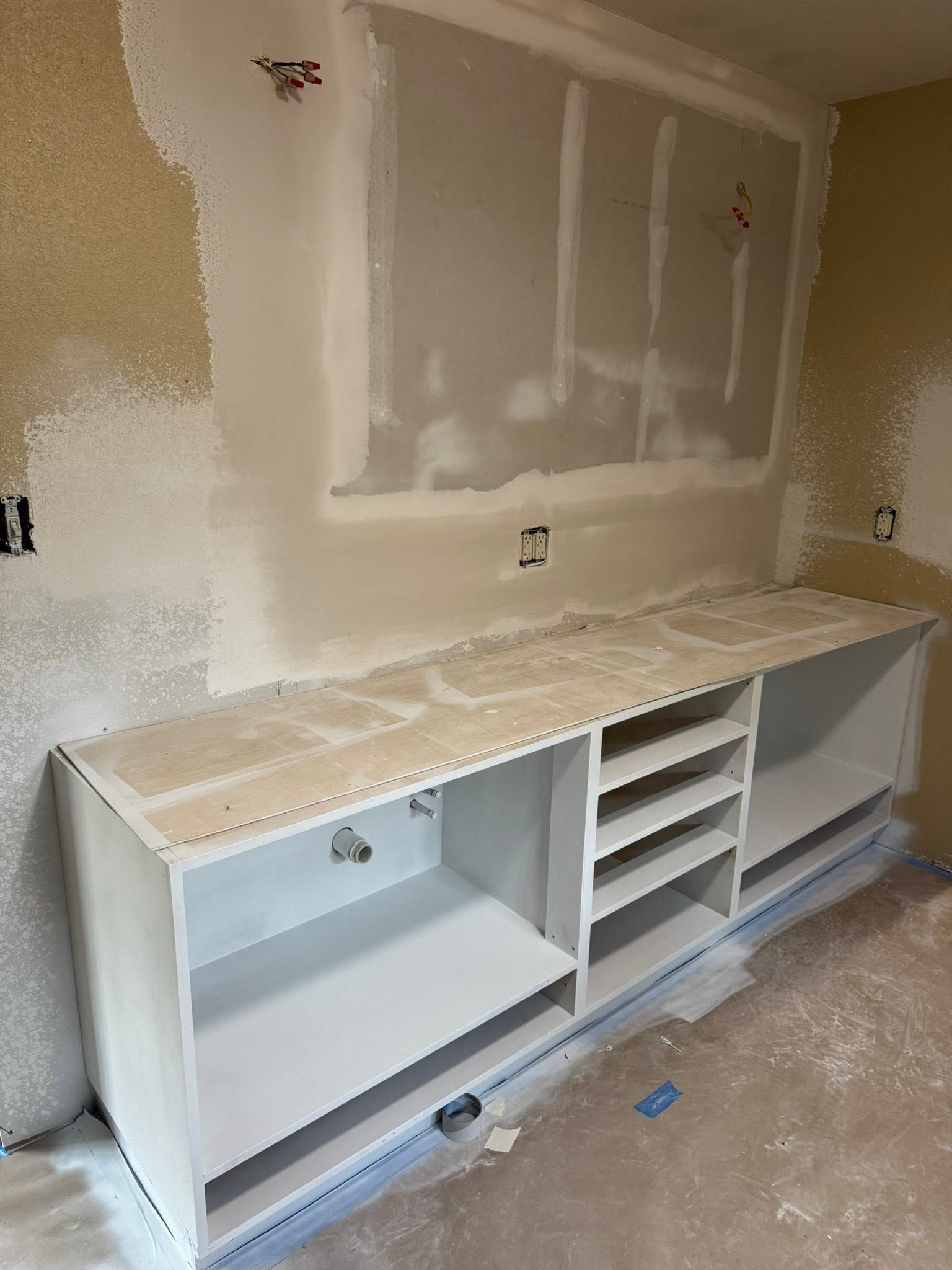 White built-in cabinet and countertop in a room under renovation, with drywall patches on the wall.