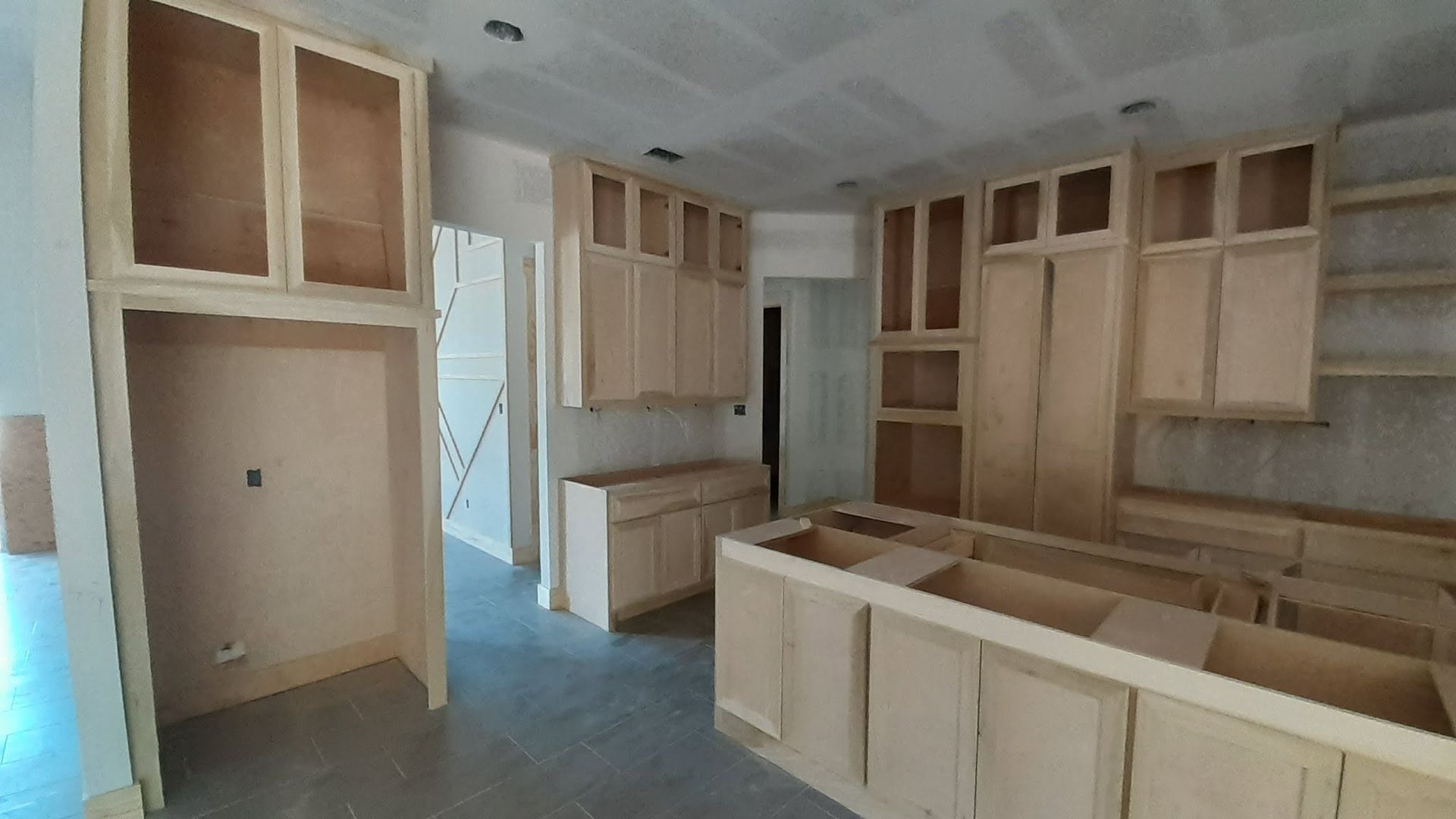Unfinished kitchen with light wood cabinets and an island in a bright room