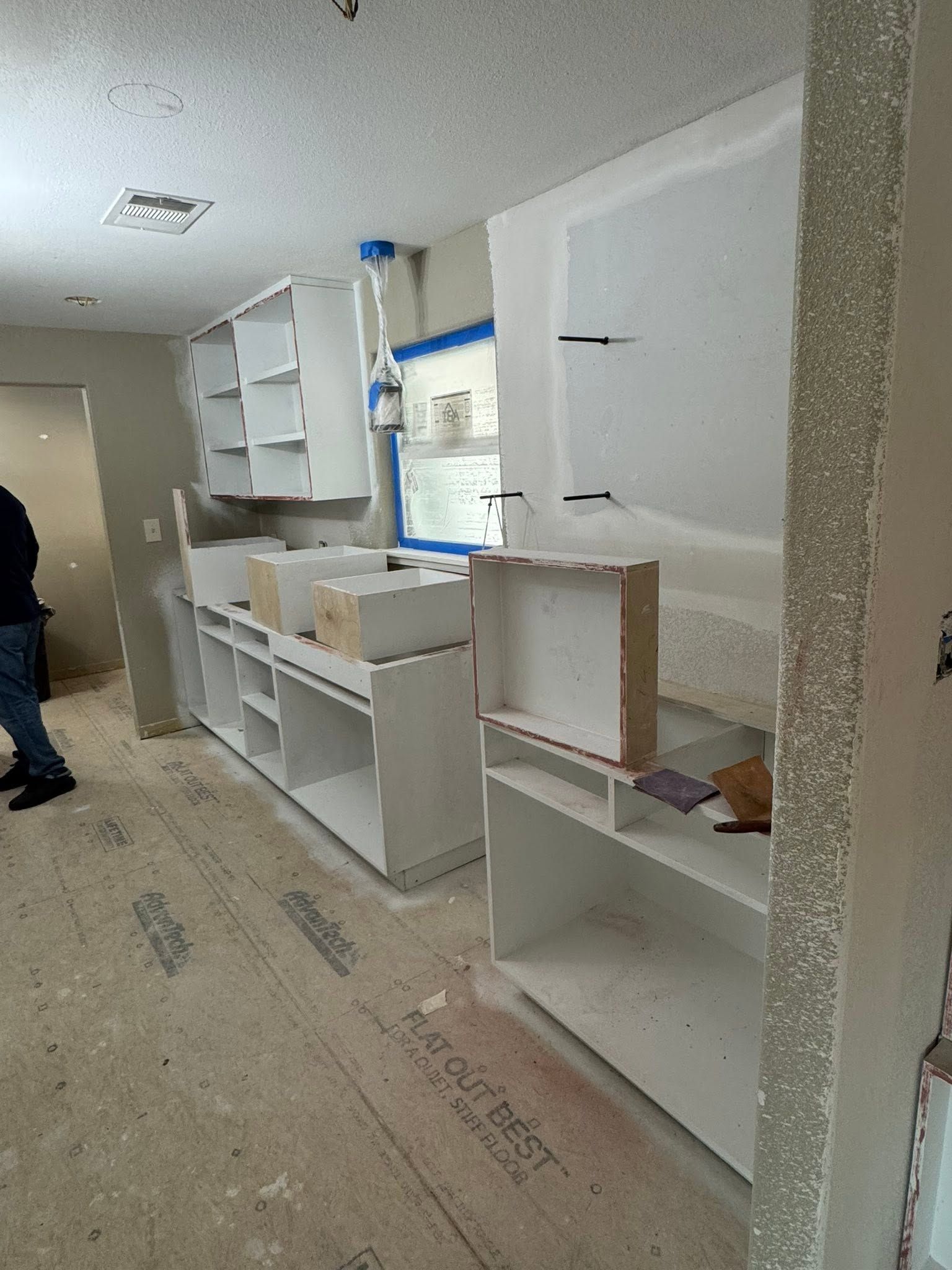 Partially renovated kitchen with white cabinets, countertops, and a window under construction