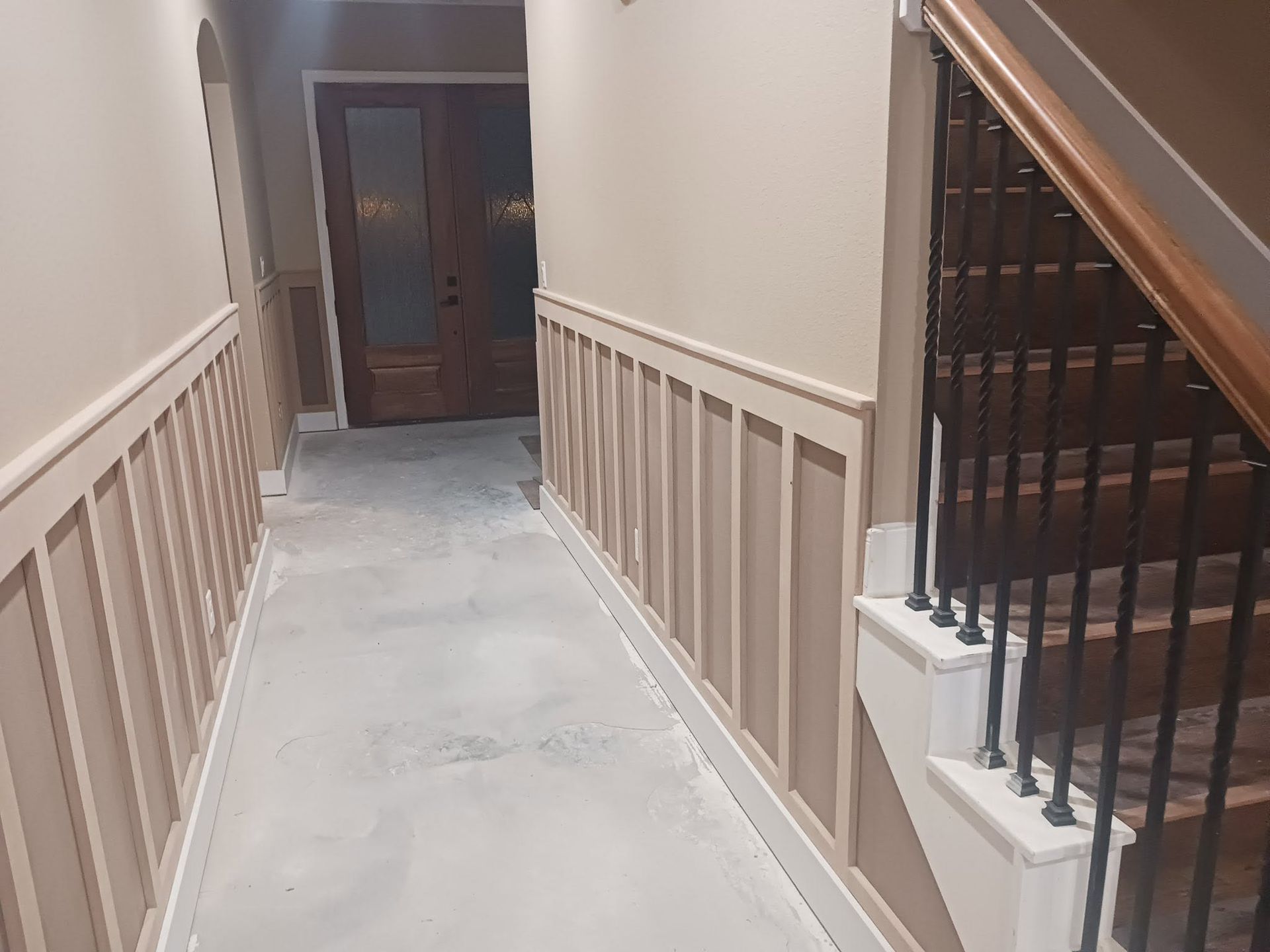 Narrow indoor hallway with beige walls, white railing, and dark wooden door at the end