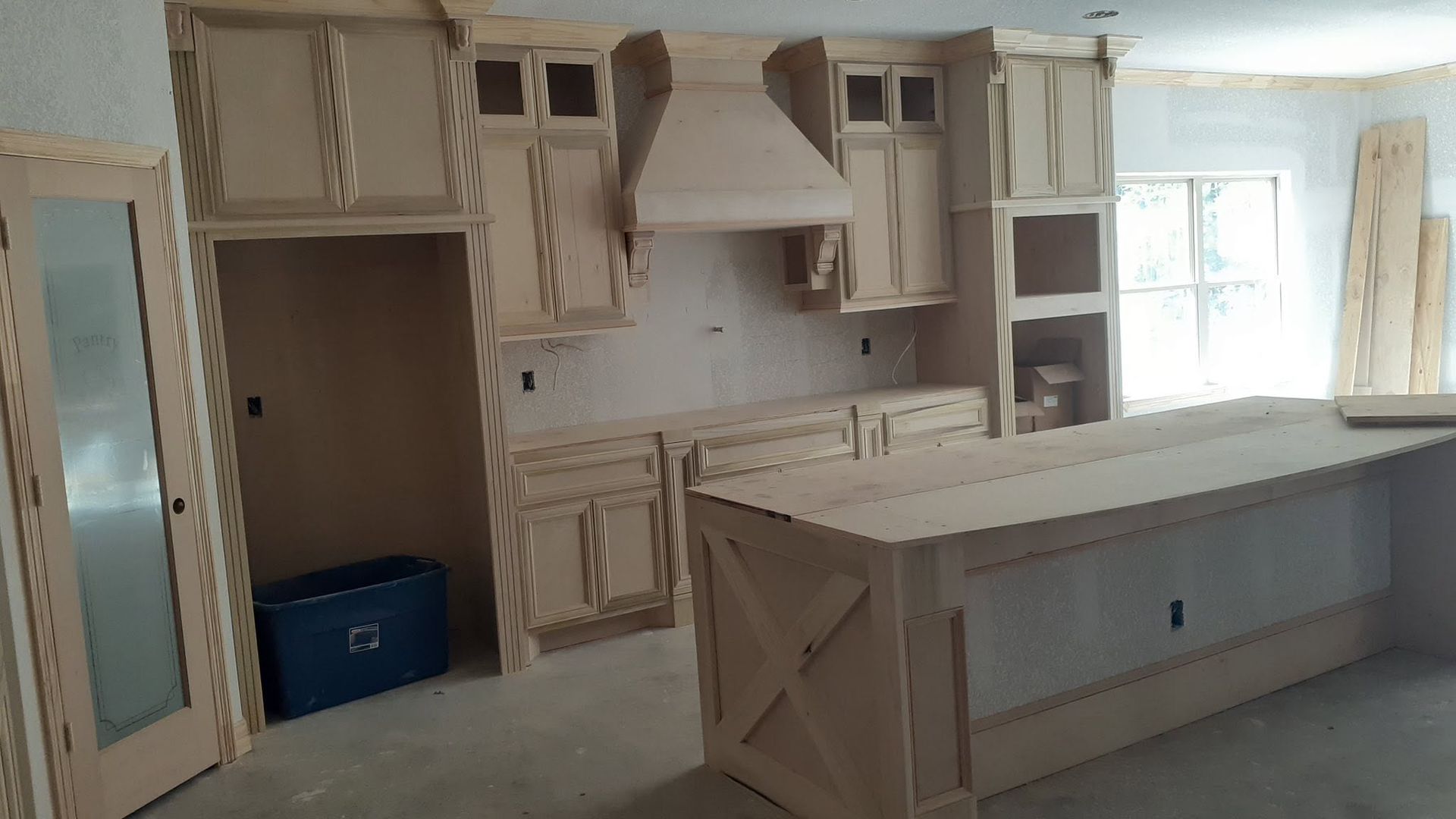 Unfinished kitchen with white cabinets, a large island, and a range hood under construction.