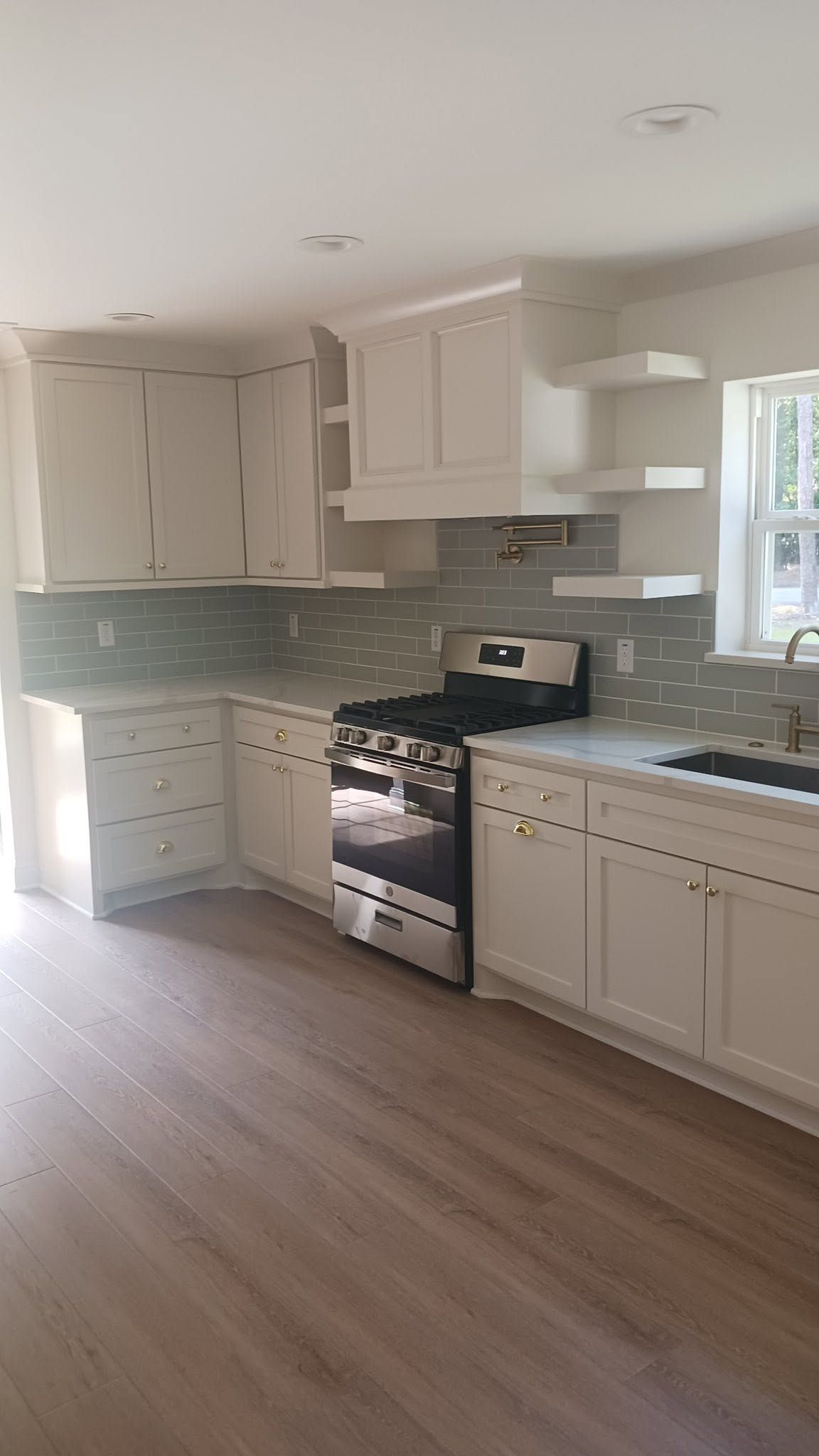 Bright white kitchen with cabinets, black stove, blue tile backsplash, and wood floors.