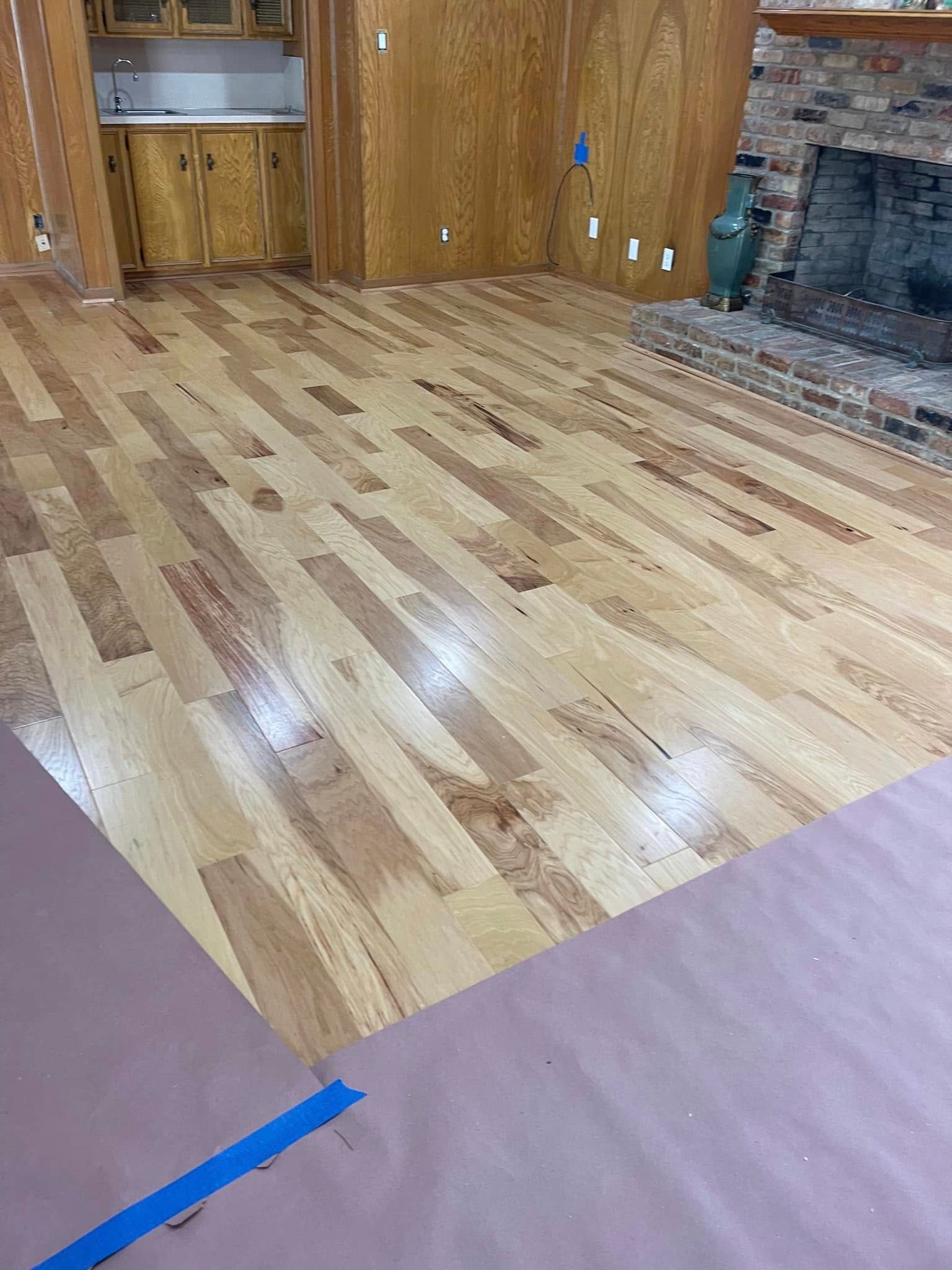 Empty room with hardwood floor, wood-paneled walls, and a stone fireplace.