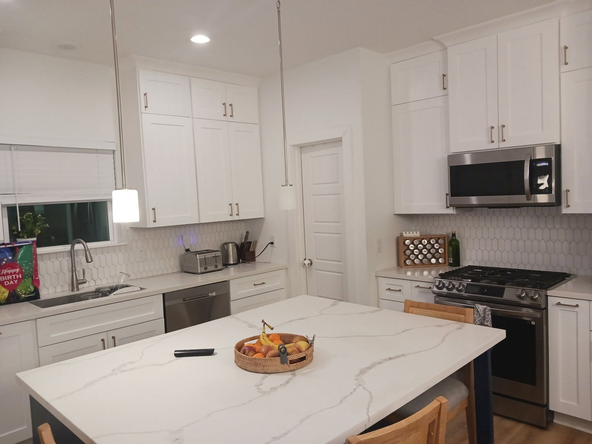 Bright white kitchen with marble island, stainless appliances, and a bowl of fruit on the counter.