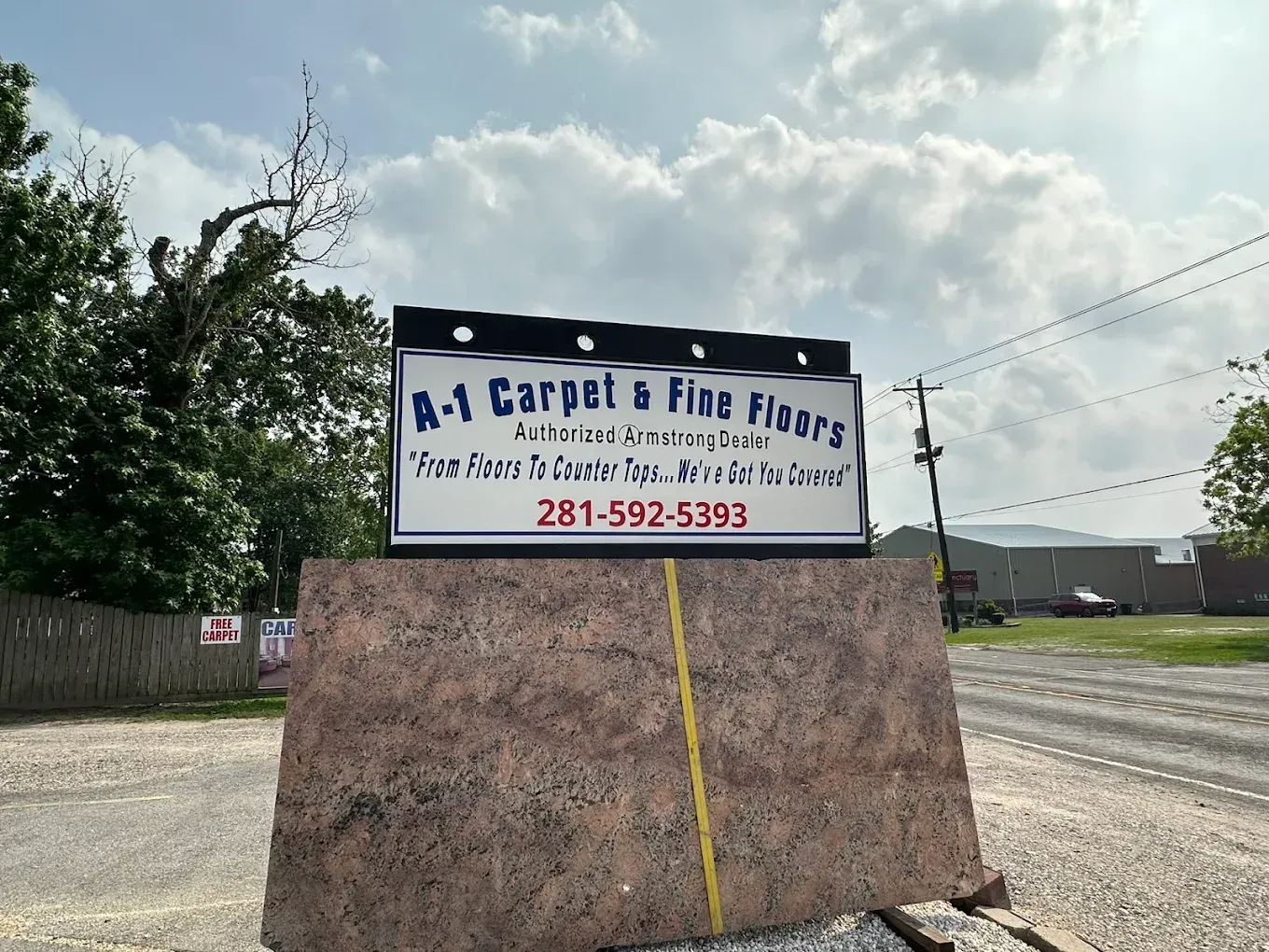 Roadside carpet sign on a weathered board with a phone number, under a cloudy sky.