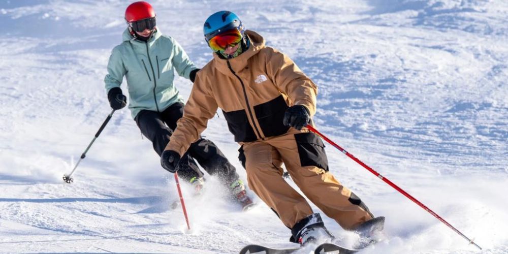Two people are skiing down a snow covered slope.