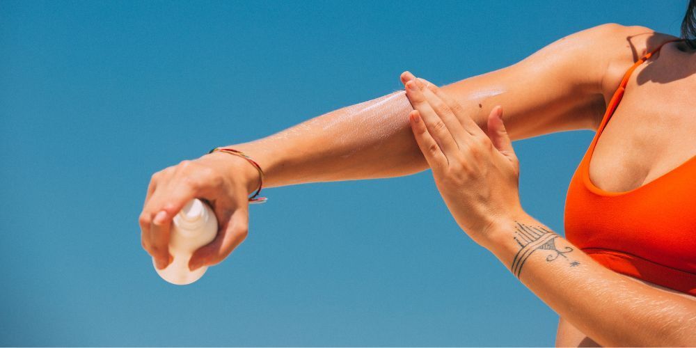 A woman in a bikini is applying sunscreen to her arm.