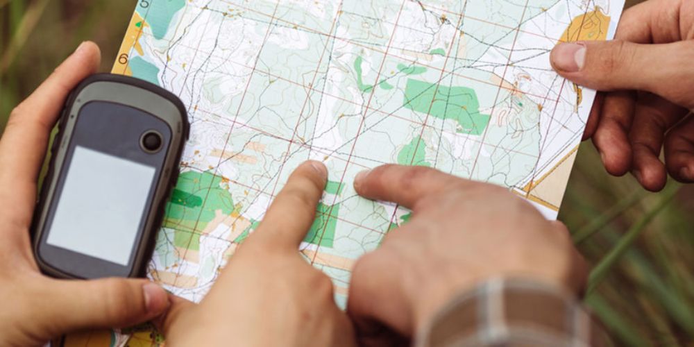 A person is holding a gps and pointing at a map.