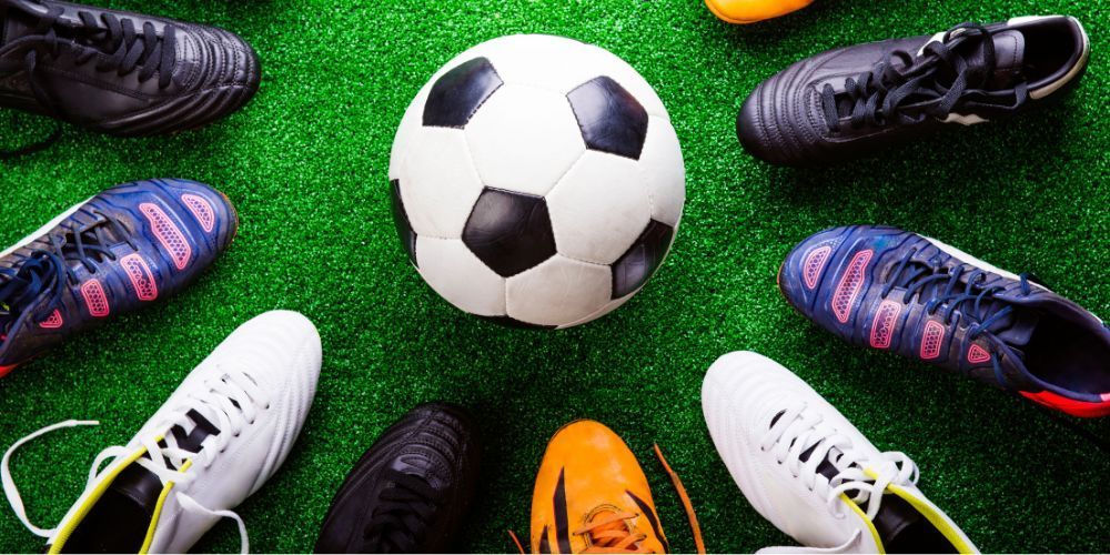 Soccer ball surrounded by several pairs of cleats on a green field.
