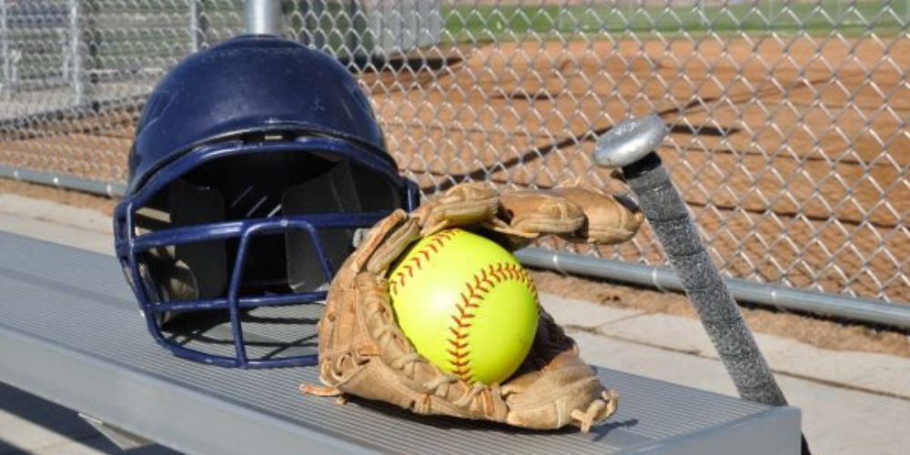 A softball glove , helmet and bat are on a bench.