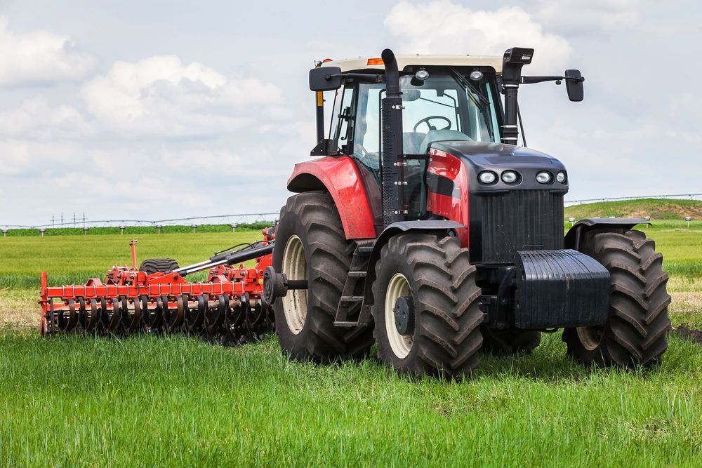 Red Tractor Plowing a Green Field With a Disc Harrow Attachment — Paul’s Tyres & Farm Maintenance in Orange, NSW