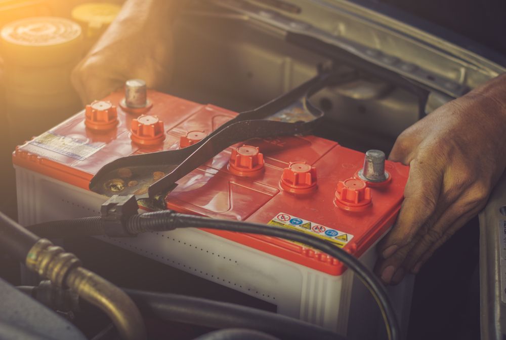 Hands Installing a Red Car Battery in an Engine Bay — Paul’s Tyres & Farm Maintenance in Gilgandra, NSW