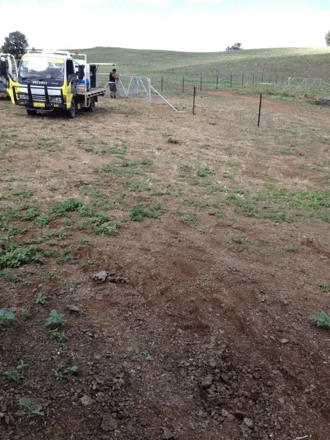 A Yellow Truck and Two People Are Setting Up a Fence in a Field — Paul’s Tyres & Farm Maintenance in Apsley, NSW