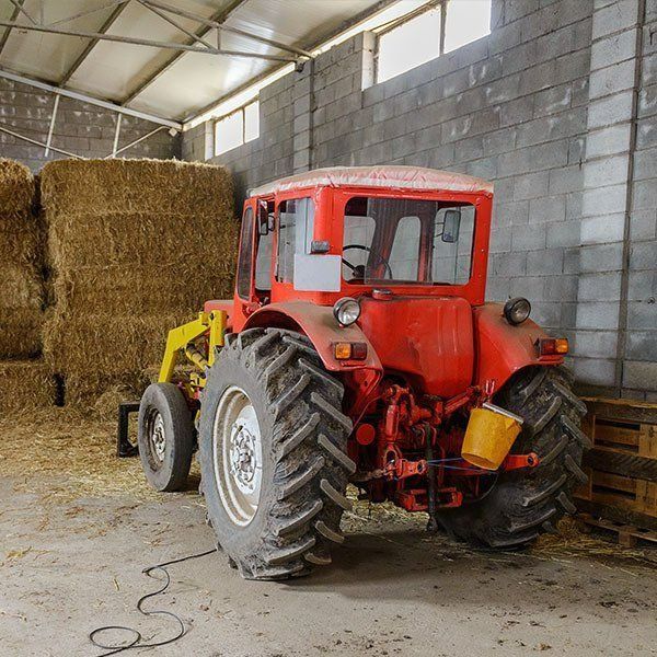 Red Tractor Parked Inside a Barn Next to Hay Bales — Paul’s Tyres & Farm Maintenance in Apsley, NSW