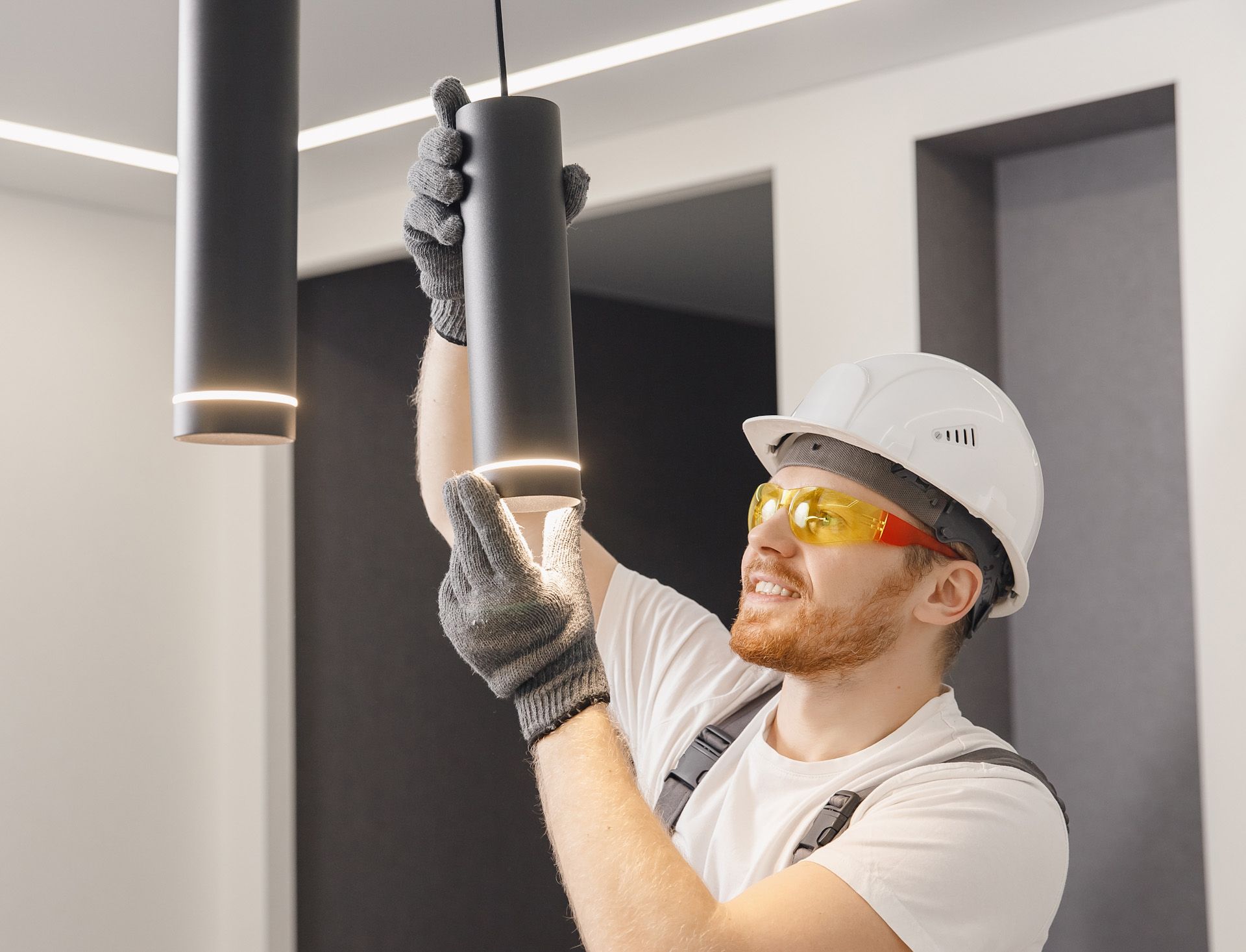 A man wearing a hard hat and safety glasses is installing a light fixture.