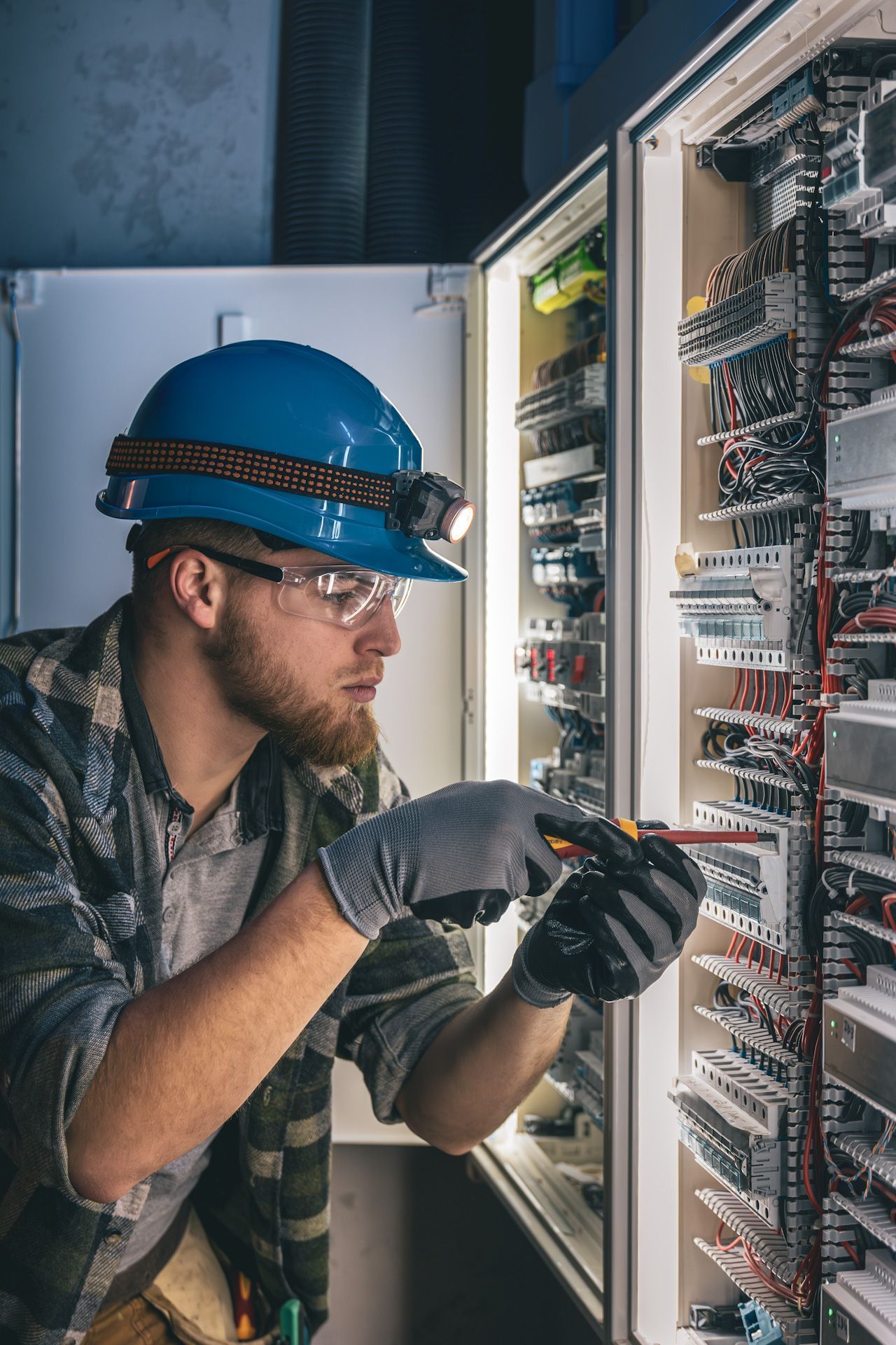 A man wearing a hard hat and safety glasses is working on an electrical panel.