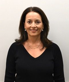 A woman wearing a necklace and earrings is smiling for the camera.