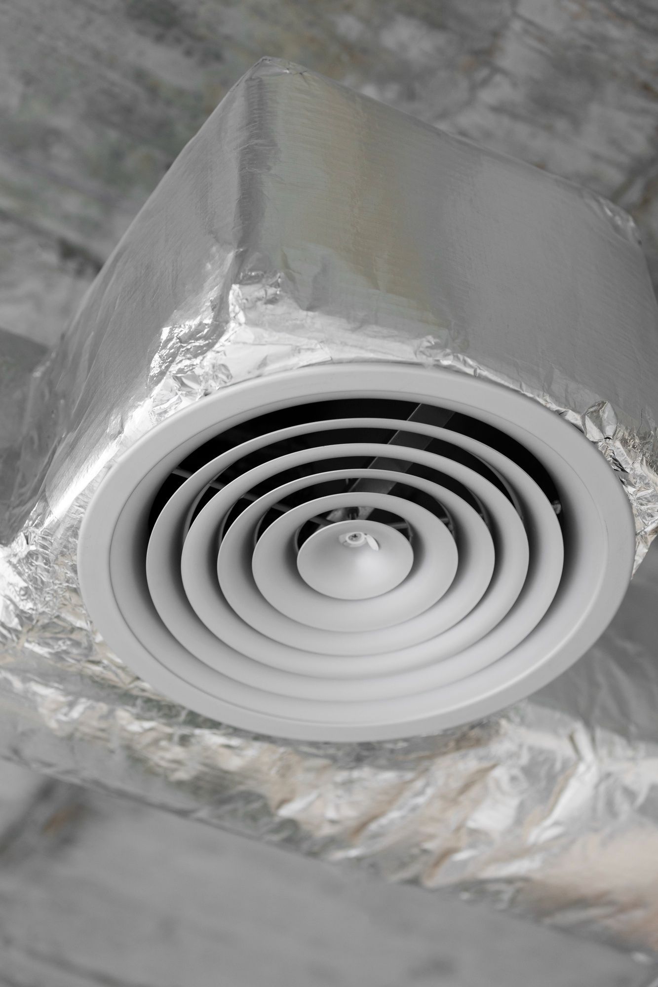 A close up of a white air vent wrapped in aluminum foil.
