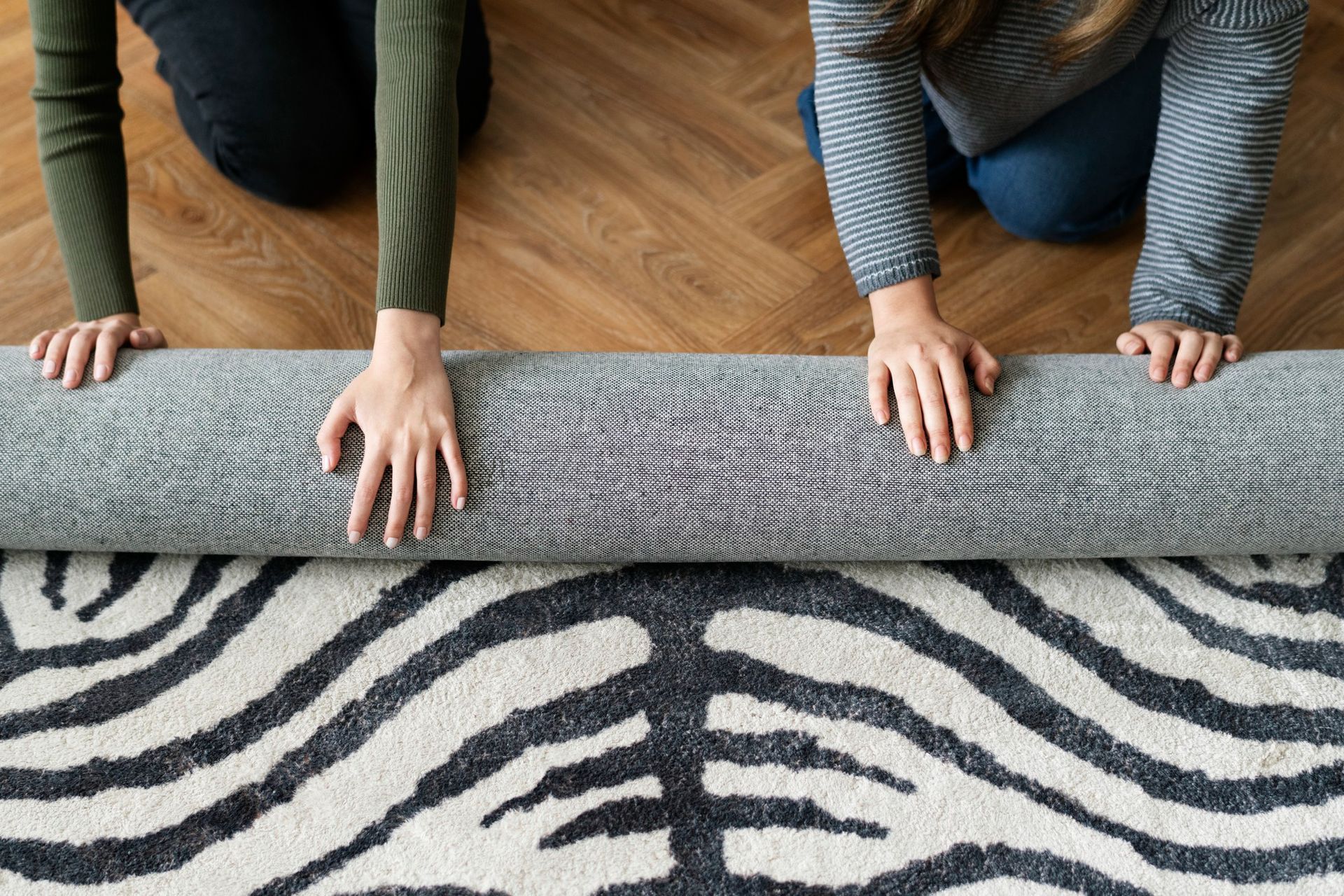 Two people are rolling a rug on the floor.