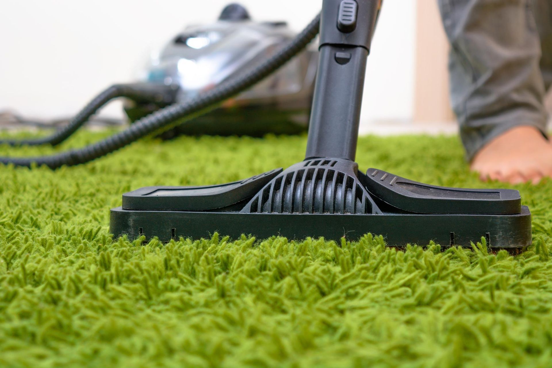 A person is using a vacuum cleaner to clean a green carpet.