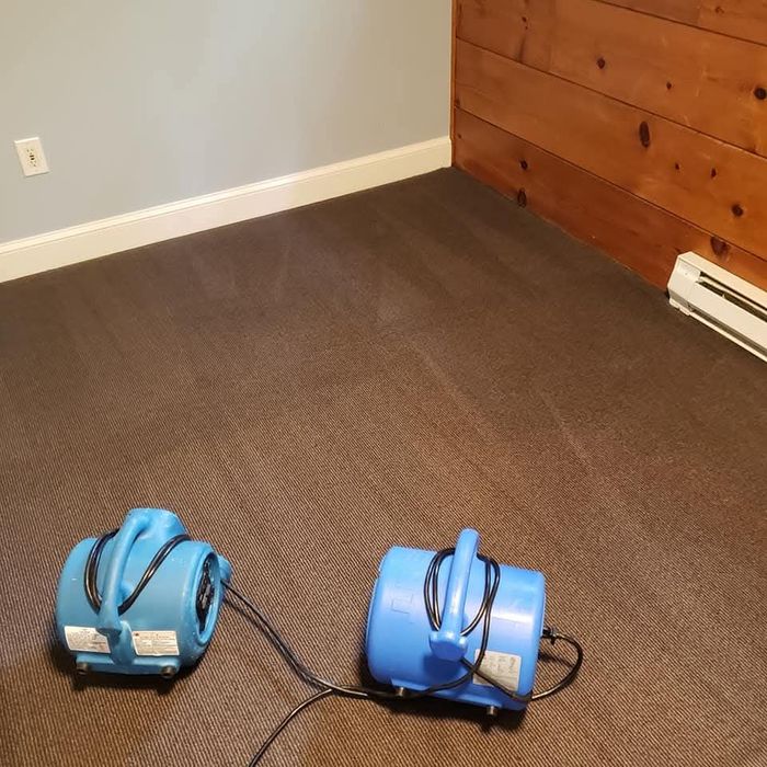 Two blue air movers on carpet in an empty room with gray walls and wood paneling.