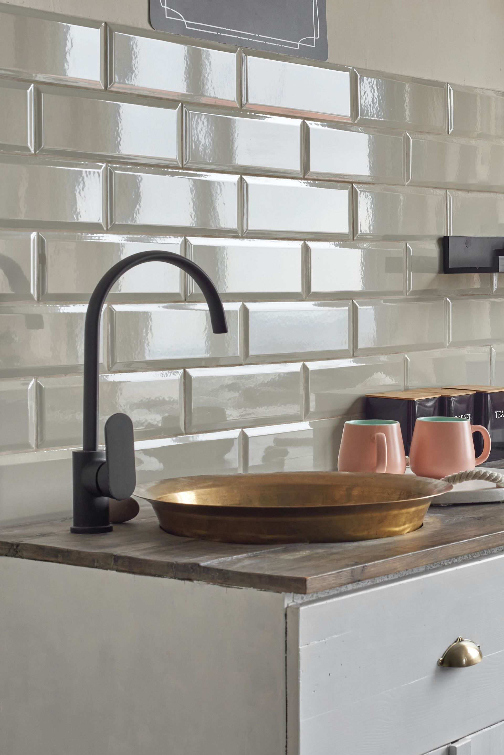 Black faucet over a gold basin set into a wooden counter, against white subway tile backsplash.