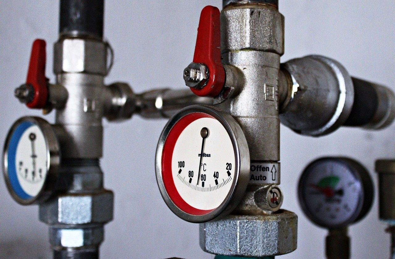 Close-up of plumbing pipes with red and blue valves, and three circular gauges with needles.