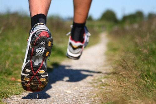 Runner's feet in athletic shoes on a dirt path, sunny outdoor setting.
