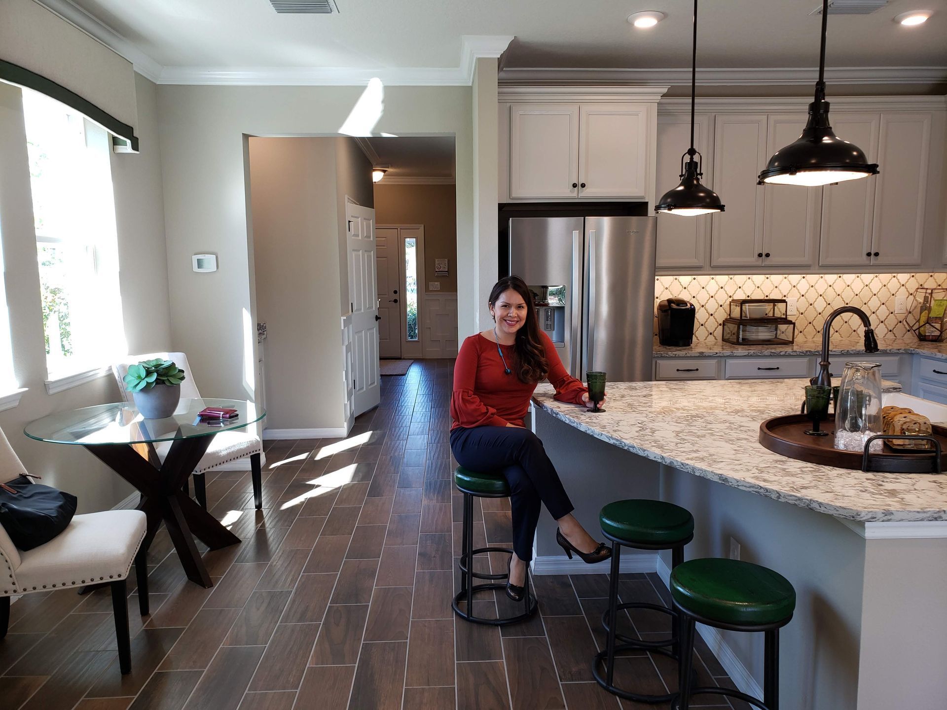 Realtor Esperanza Arias sitting on a stool in a bright kitchen with granite island and stainless steel appliances
