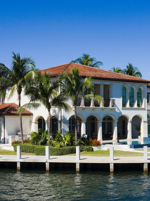 White waterfront villa with red-tiled roof and palm trees under a clear blue sky
